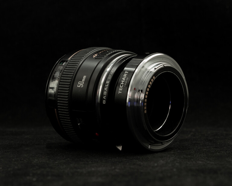 Vintage camera lens assembly with multiple glass elements and metal barrel components against dark background.