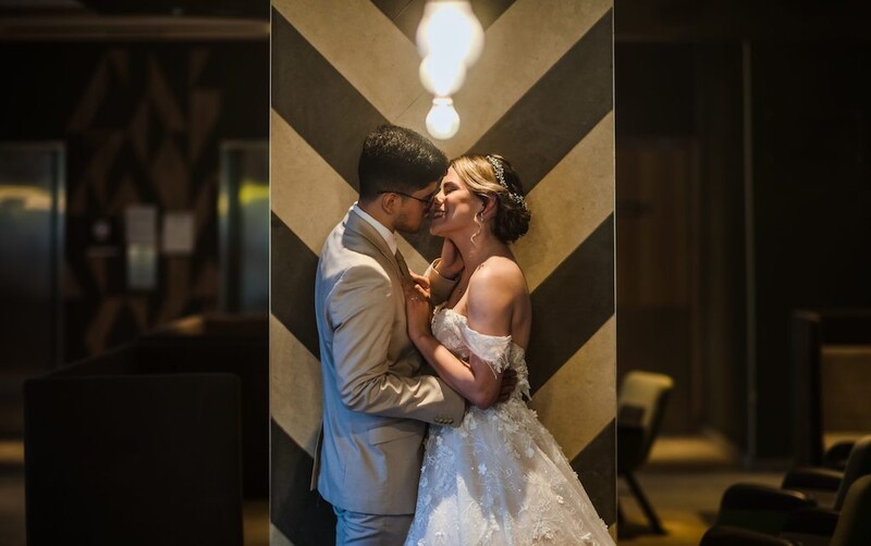 Bride and groom kissing in a modern corridor with geometric ceiling lights and chevron wall patterns.