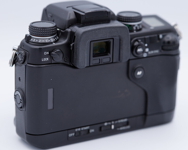 Top-down view of a digital camera body showing the viewfinder, mode dial, and control buttons on a white background.