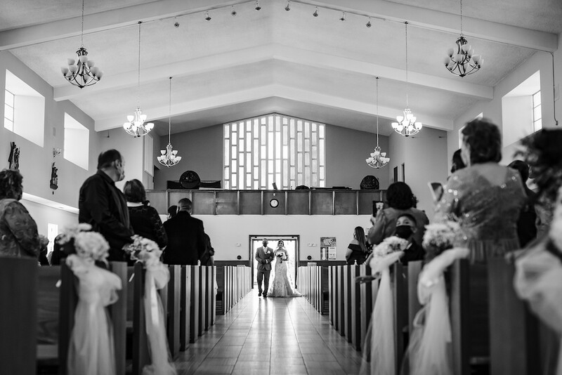 Black and white photograph of a bride walking down a church aisle toward an altar during a wedding ceremony.
