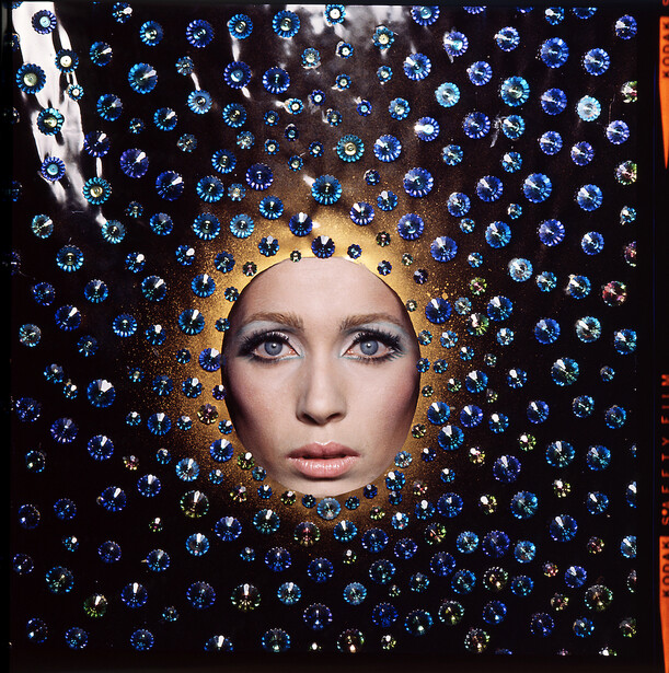 Woman's face surrounded by a spherical halo of blue crystals or gemstones against dark background.