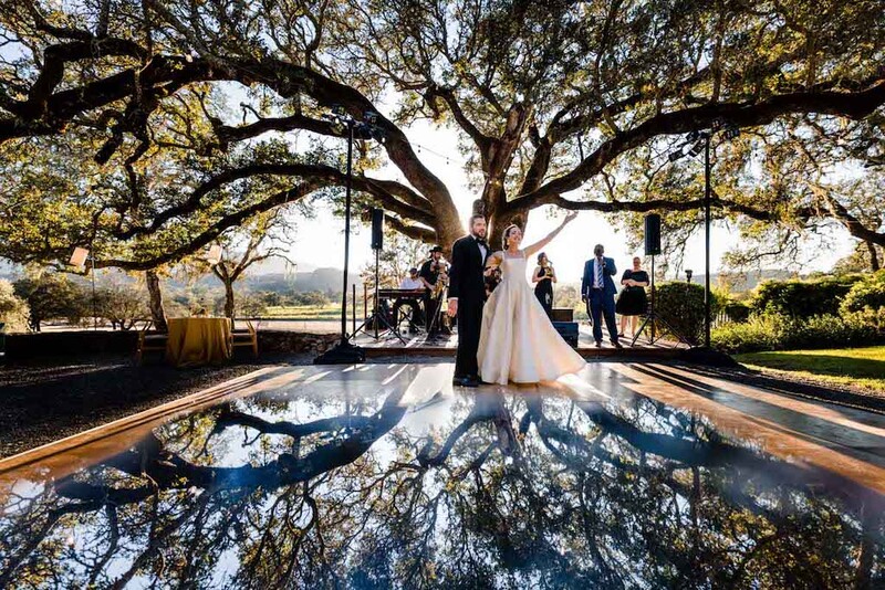 Bride and groom exchanging vows beneath a sprawling oak tree, with their reflections mirrored in a water feature below.