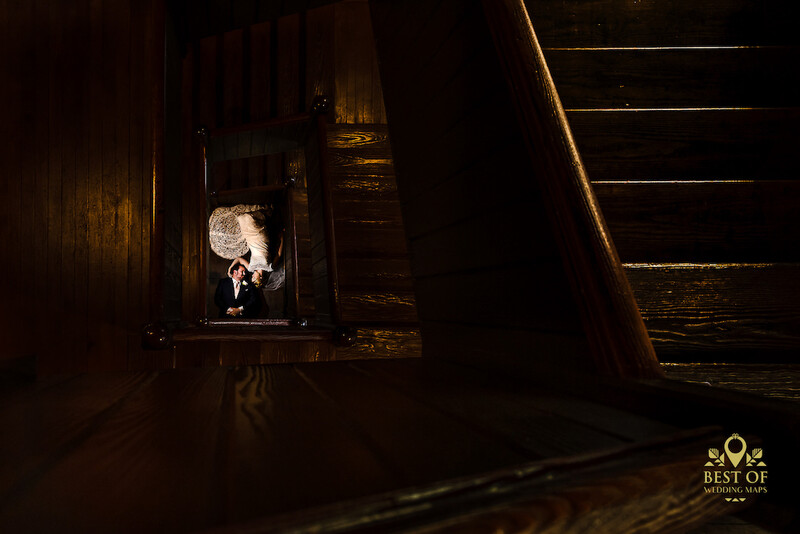 Bride in white dress photographed in dramatic backlighting within a dark wooden doorway or corridor.