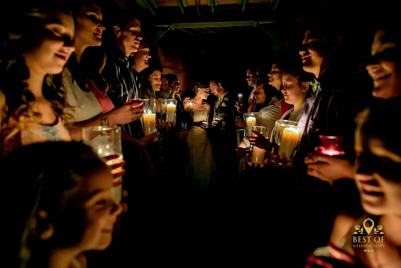 Group of people holding lit candles in a darkened space, creating warm golden light against deep shadows.