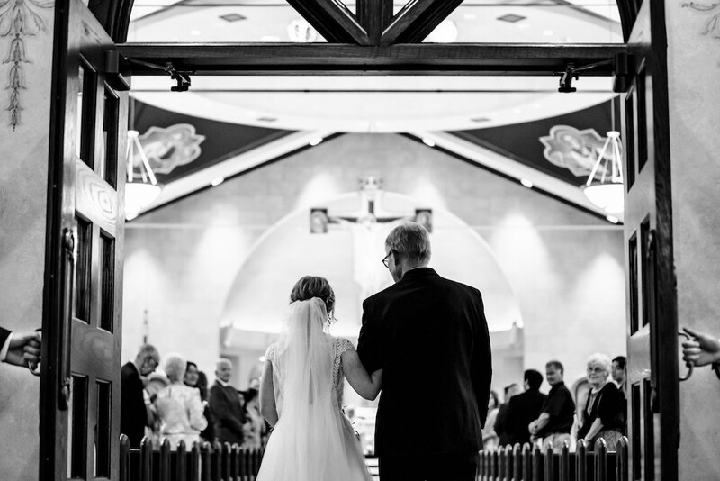 Bride and groom walking down the aisle toward the altar in a church with guests seated on either side.