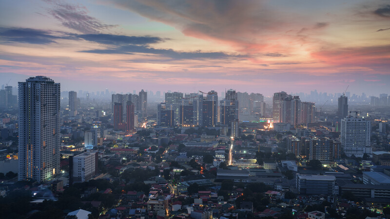 Urban skyline at twilight with illuminated buildings against a colorful sunset sky.