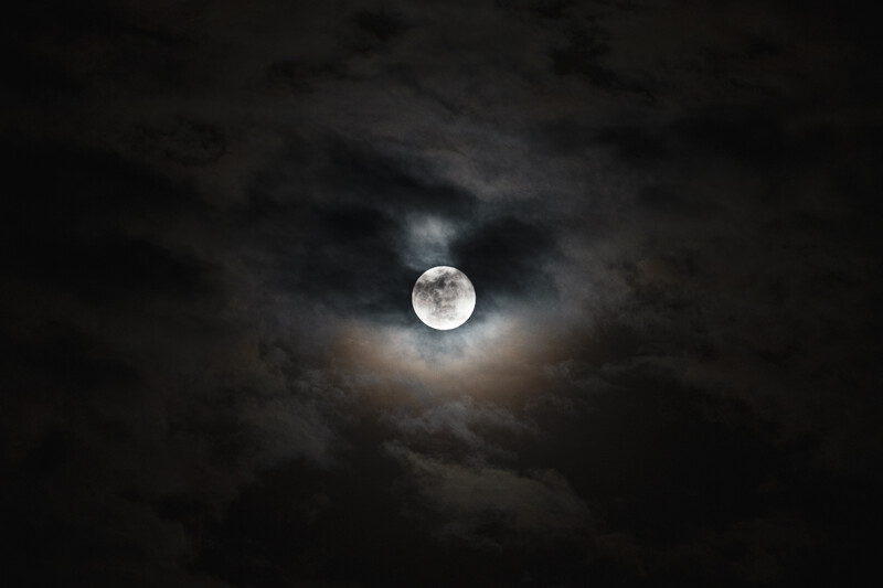Full moon glowing brightly through dark, roiling storm clouds at night.