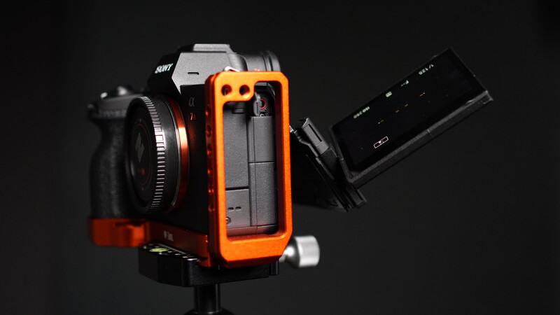 Orange and black camera mounting rig with telephoto lens and external monitor against dark background.