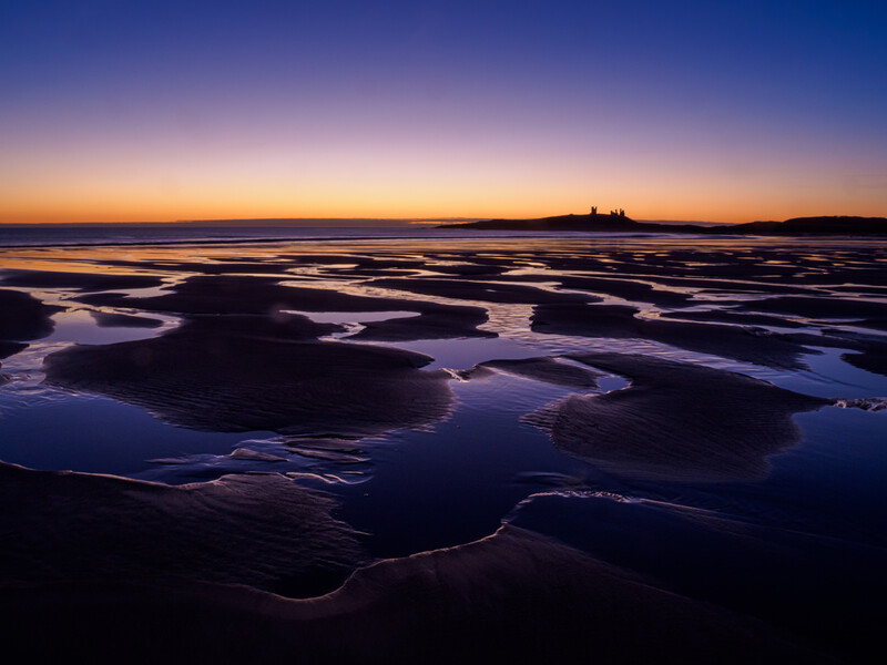 Tidal flats at twilight with winding water channels reflecting purple and blue sky.