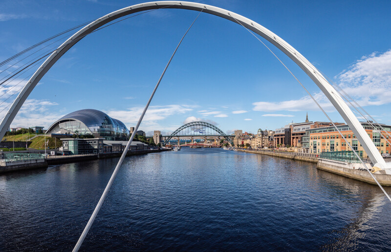 Modern white arch bridge framing a waterfront cityscape with historic bridges and dome structures.