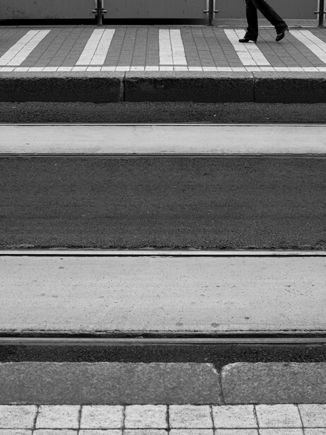 Black and white photograph of stacked horizontal steps and striped crosswalk with pedestrian silhouette above.