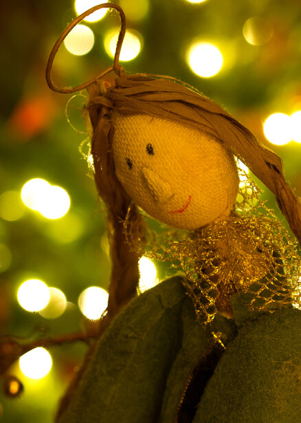 Yellow ornament with wire attachment hanging among warm-toned bokeh lights.