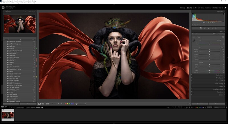 Portrait of a woman with dramatic red fabric flowing around her head and shoulders against a dark background.