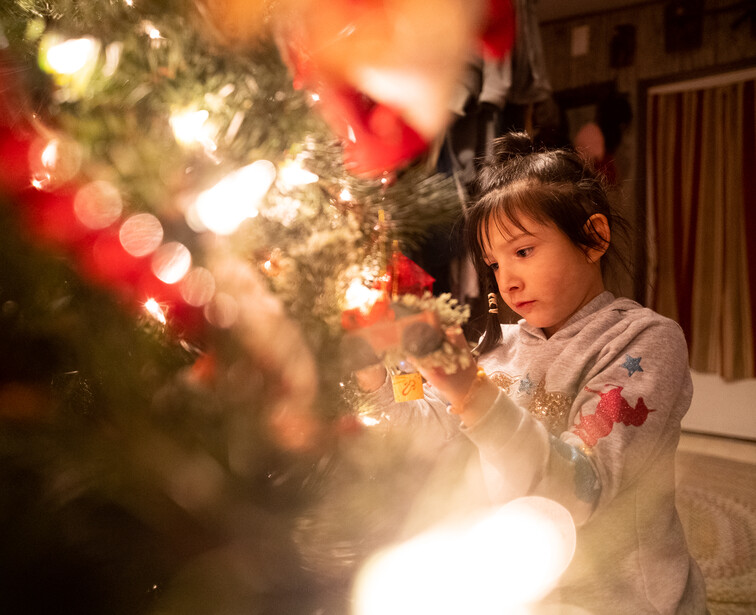 Young child gazing at illuminated Christmas tree with warm white and red lights indoors.