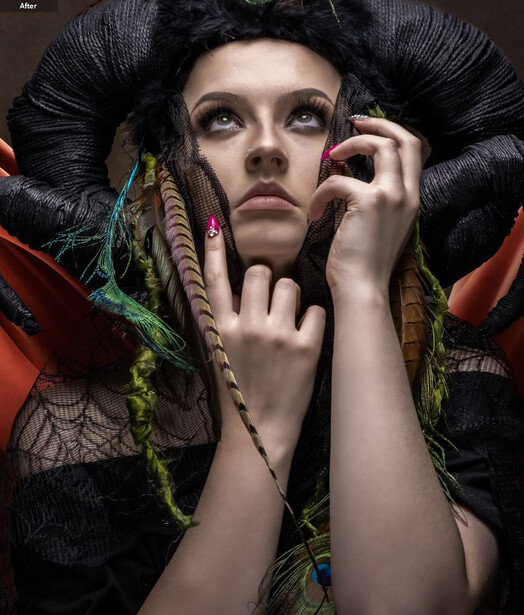 Woman with pale makeup and dramatic black feathered headdress, hands framing face with colorful beaded braids.