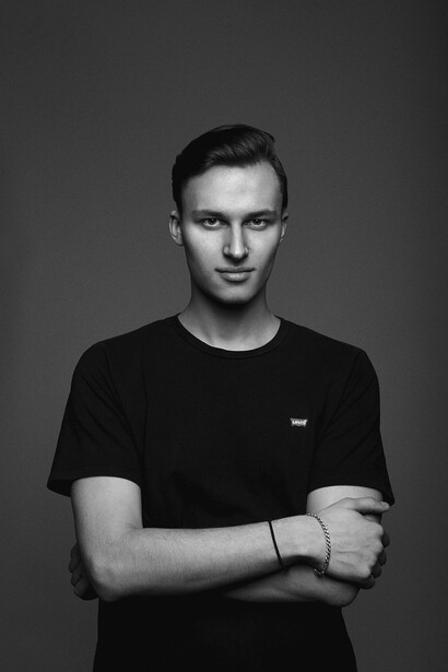Black and white portrait of a young man wearing a dark t-shirt with arms crossed, looking directly at camera.