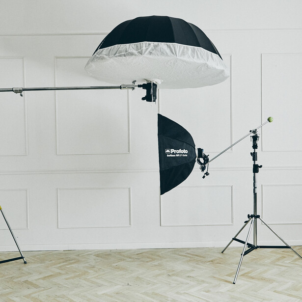 Studio lighting setup with parabolic umbrellas and light stands against white wall backdrop.