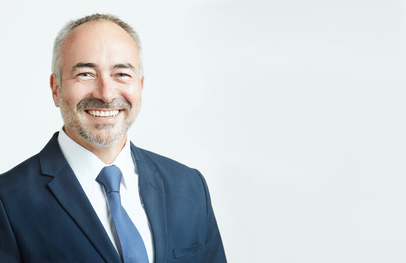 Professional headshot of a smiling man in a dark blue suit and tie against a plain white background.