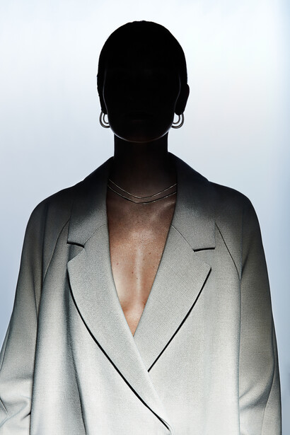 Silhouetted figure wearing an oversized light gray blazer against a neutral background.