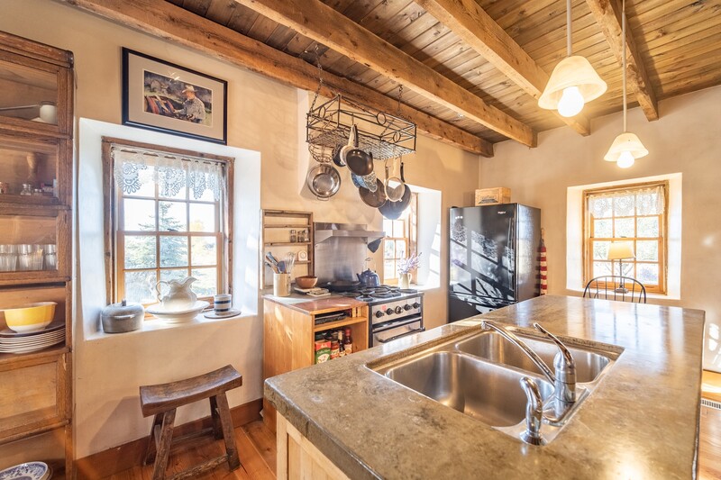 Warm-toned kitchen interior with exposed wooden beams, stainless steel sink, and natural light from multiple windows.