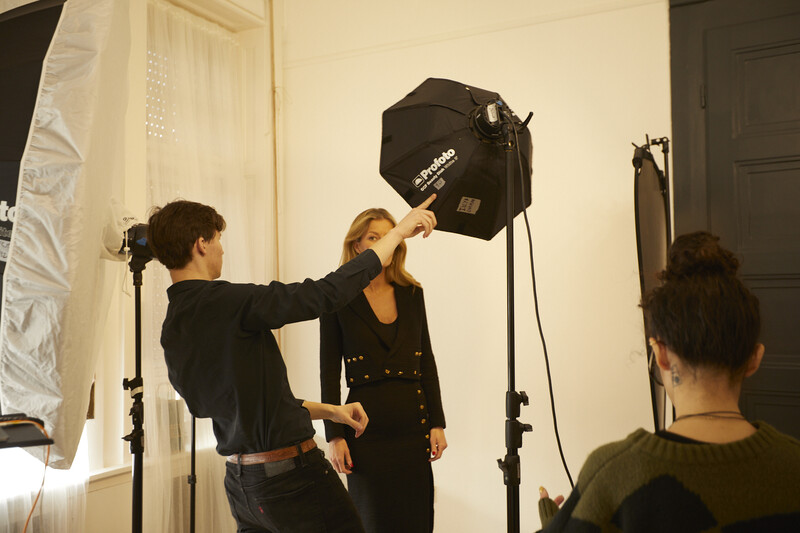 Photographer adjusting a softbox light while a model stands positioned in front of the setup during a studio shoot.