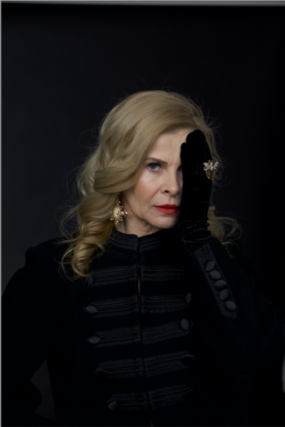 Woman with blonde wavy hair wearing black turtleneck against dark background.