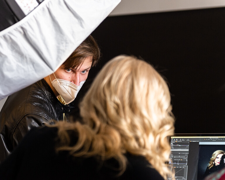 Photographer adjusting a large white reflector or diffusion panel during a portrait shoot with a subject in foreground.