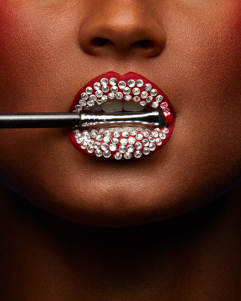 Close-up of lips decorated with rhinestones and a black brush stroke across the mouth.