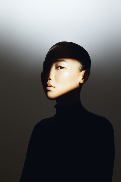 Person in black turtleneck and cap photographed against gradient gray background with directional lighting.