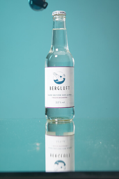 Bergluft bottle with reflection on turquoise background, minimalist product photography setup.