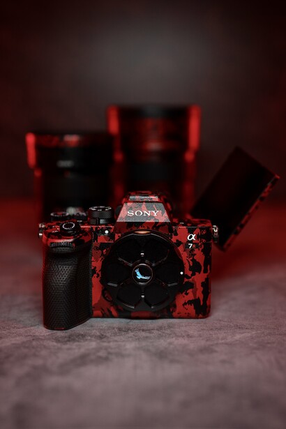 Red DSLR camera with telephoto lenses arranged on dark surface against deep red background.