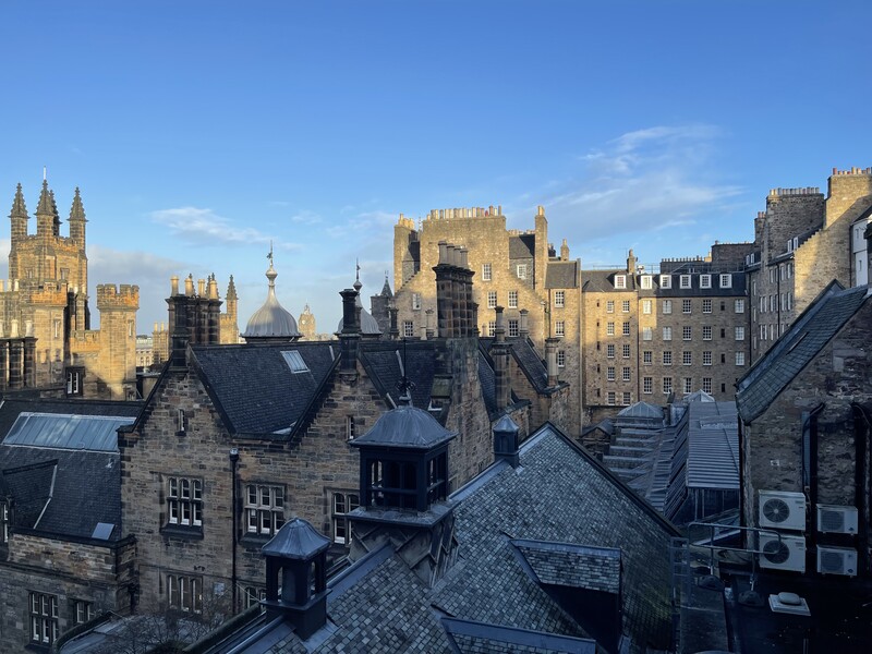 Aerial view of historic stone buildings with steep roofs overlooking a cityscape of spires and towers.