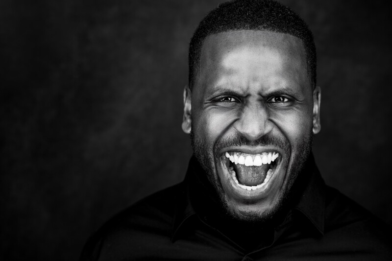 Black and white portrait of a man with an exuberant, wide smile against a dark background.