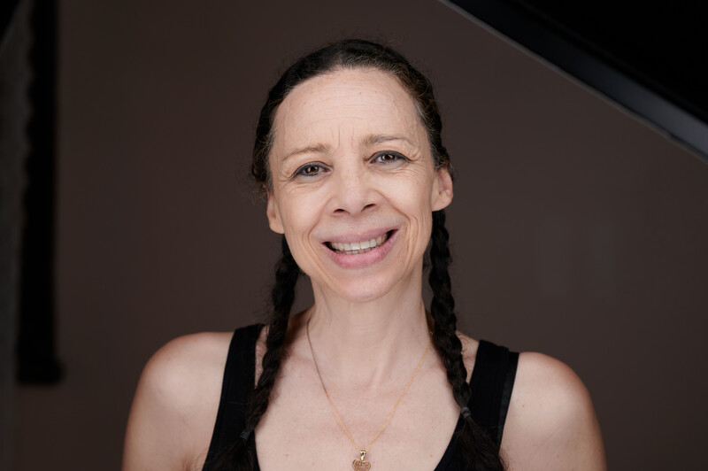Woman with dark braided hair smiling at camera against brown background.