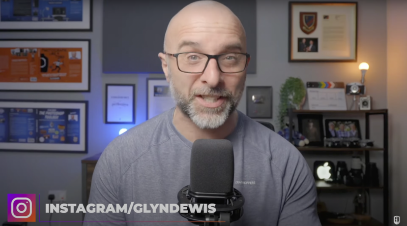 Man wearing glasses speaking into a microphone in a home office studio setup.