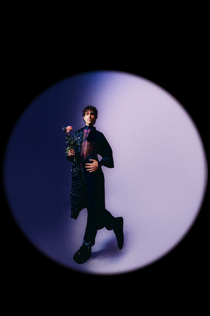 Person in dark clothing posing against a circular gradient background that transitions from deep blue to pale lavender.