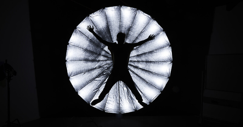 Silhouette of a figure with arms raised within a circular light source against a dark background.