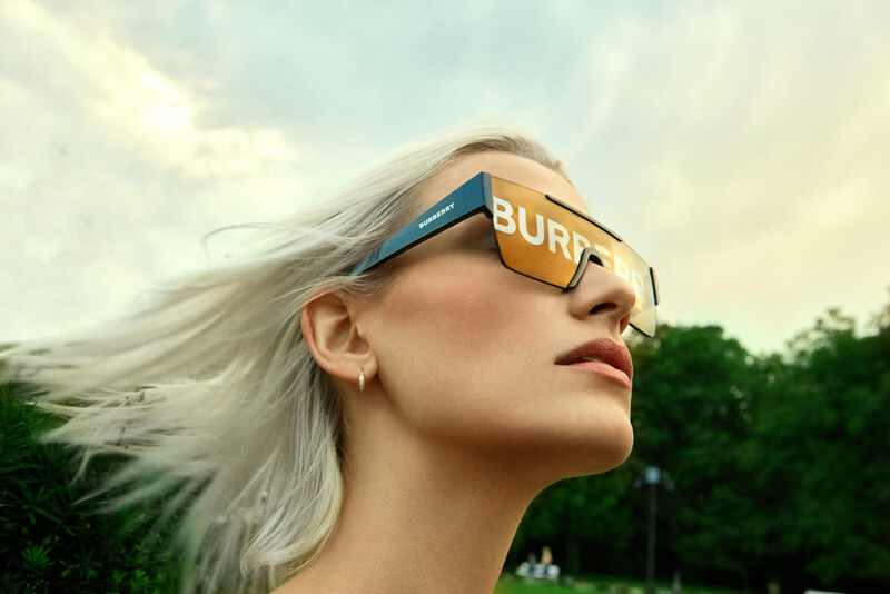 Woman wearing oversized blue and yellow sunglasses with long platinum blonde hair flowing in the wind.