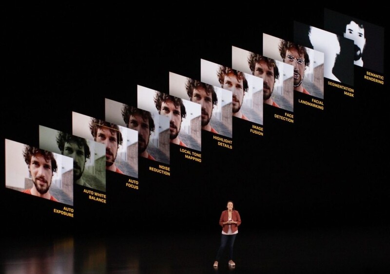 Speaker standing on stage beneath a diagonal array of illuminated portrait panels against a dark background.