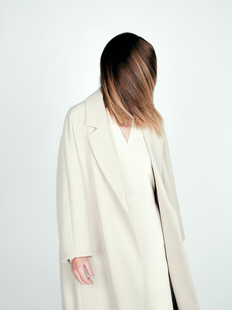 Woman in cream-colored oversized blazer photographed from behind against white background.