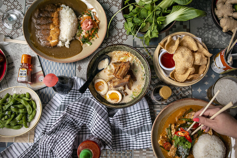 Overhead view of multiple dishes with rice, proteins, and vegetables arranged on a checkered cloth table.