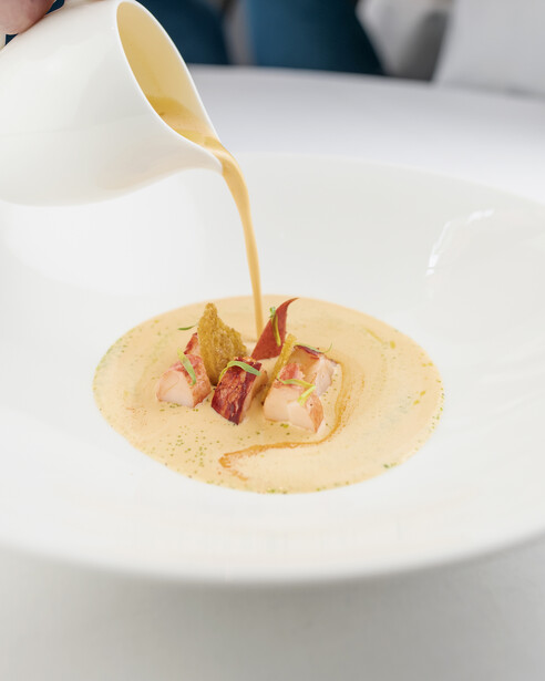 Creamy sauce being poured over a plated dish with shrimp and vegetables on a white plate.