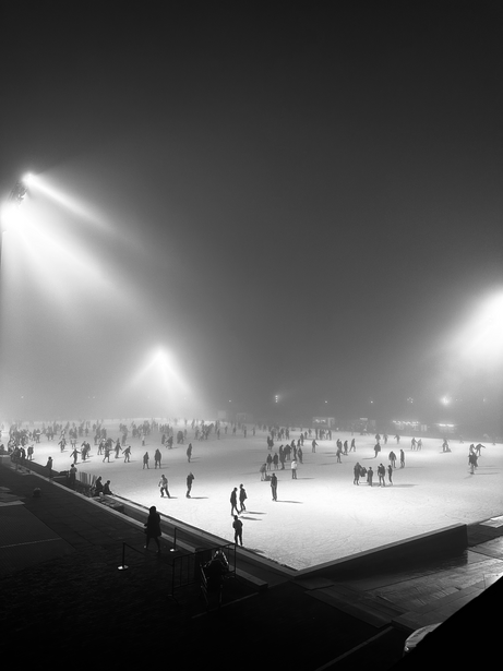 Nighttime ice skating rink filled with silhouetted skaters under bright floodlights in black and white.