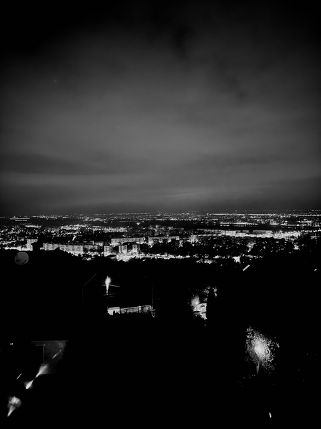 Nighttime cityscape with scattered lights across a sprawling urban area beneath an overcast sky.