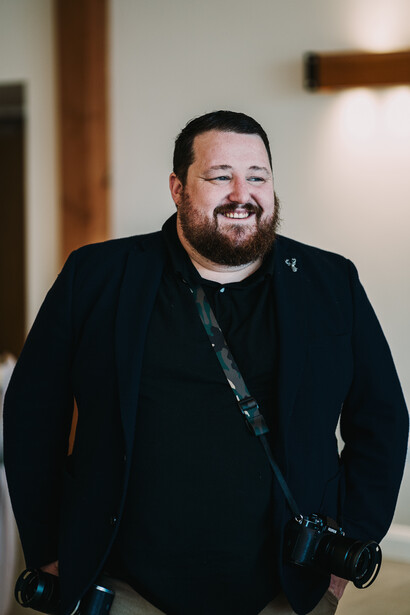 Professional headshot of a man in a black blazer smiling at the camera indoors.