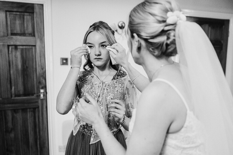Bride in veil adjusting earrings while bridesmaid assists with getting-ready preparations.