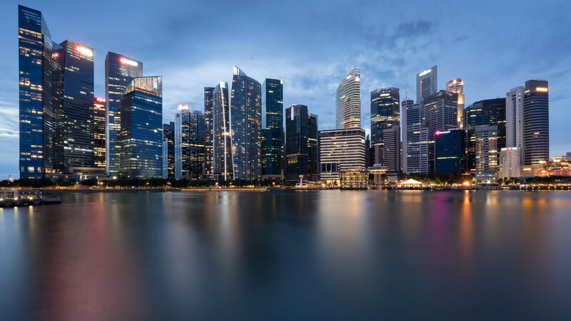 Illuminated downtown skyline reflected in calm waterfront at twilight.