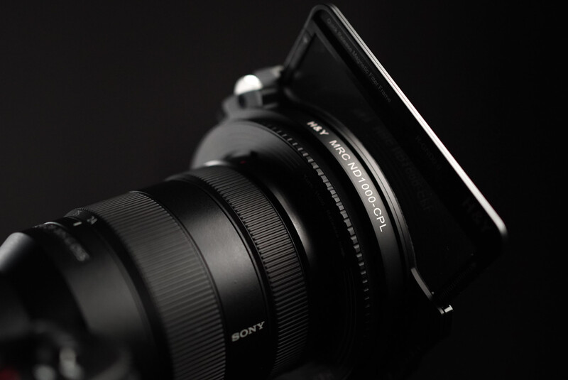 Sony lens with square filter holder mounted on camera body, photographed against dark background.