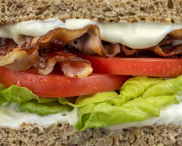 Cross-section of a BLT sandwich showing bacon, lettuce, tomato, and mayo on whole wheat bread.