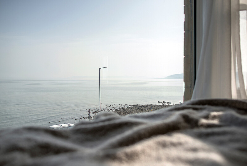 Blurred rock in foreground with calm sea, street lamp, and distant shoreline in soft focus.